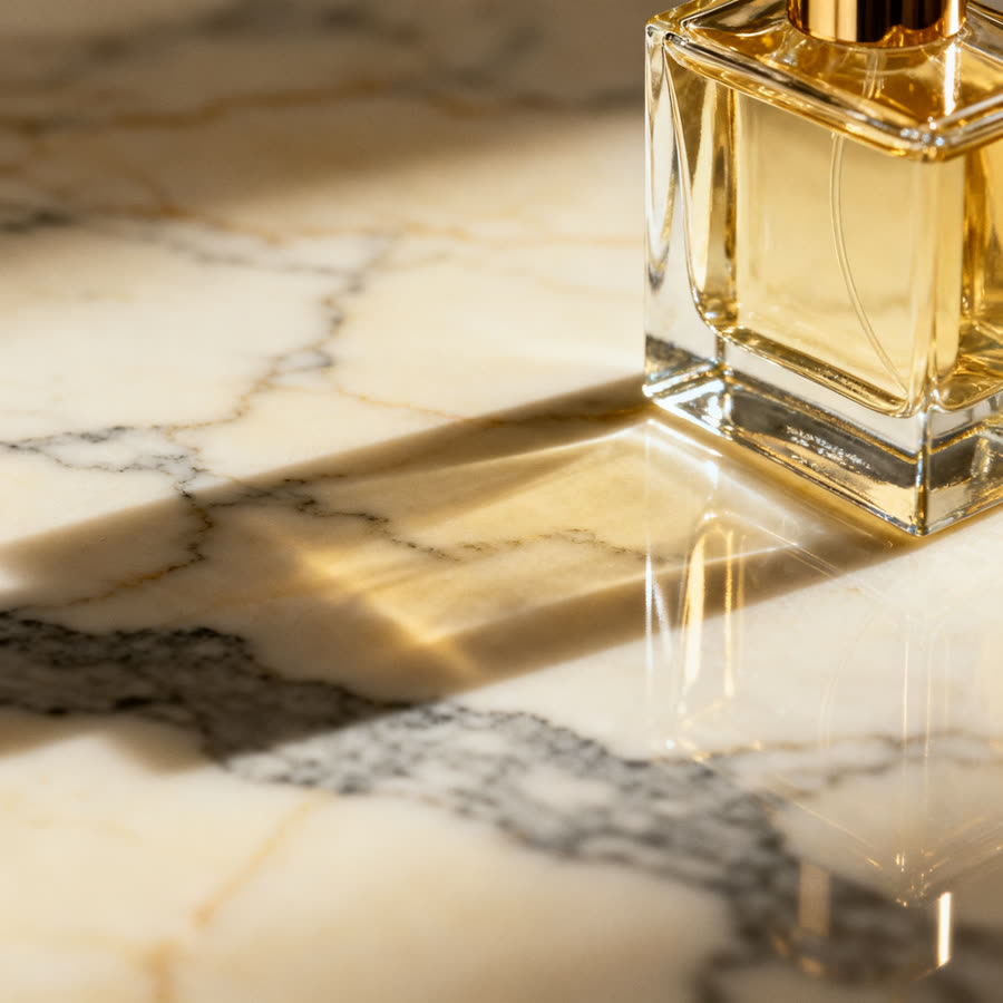 Flacon de parfum ambré posé sur du marbre, lumière rasante